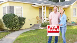Homeowners stand in front of their home with a 'For Sale' sign Homeowners stand in front of their home with a 'For Sale' sign