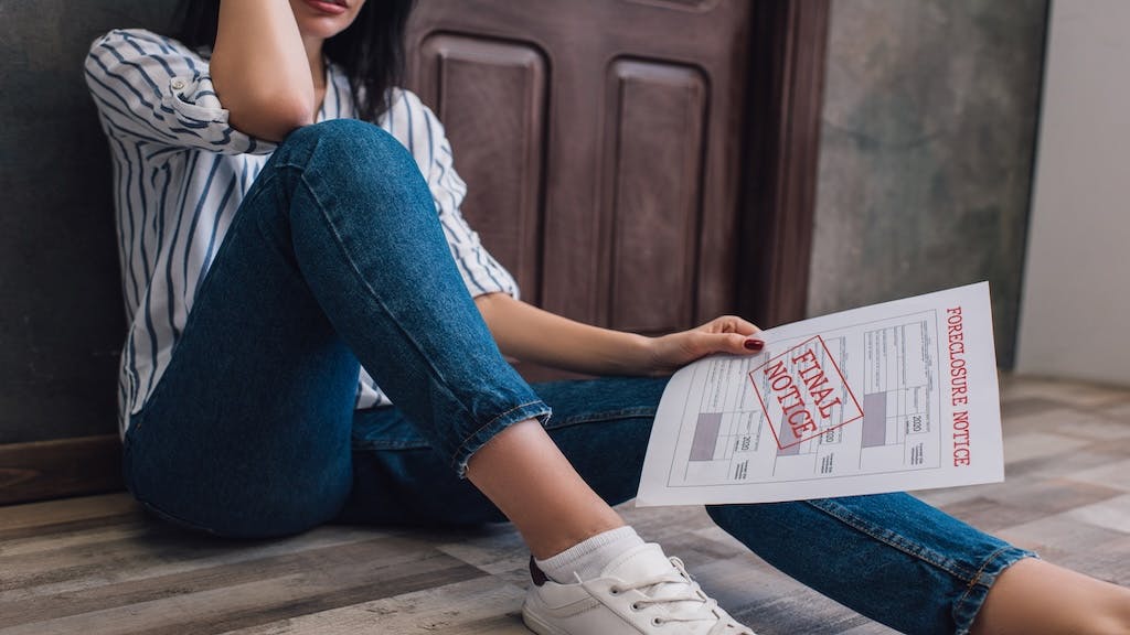 A woman sits on the floor looking over a foreclosure notice