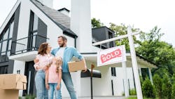 A family stands outside their recently purchased home next to a sign that reads 'Sold.' A family stands outside their recently purchased home next to a sign that reads 'Sold.'