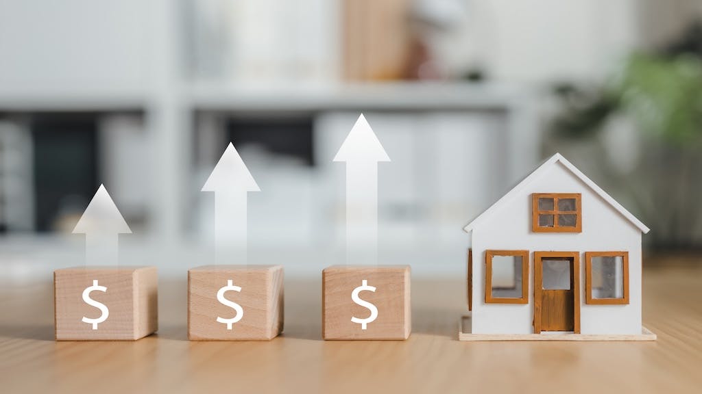 A row of blocks with dollar signs stand next to a model home. Above the blocks are arrows, showing home prices are growing.
