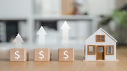 A row of blocks with dollar signs stand next to a model home. Above the blocks are arrows, showing home prices are growing. A row of blocks with dollar signs stand next to a model home. Above the blocks are arrows, showing home prices are growing.