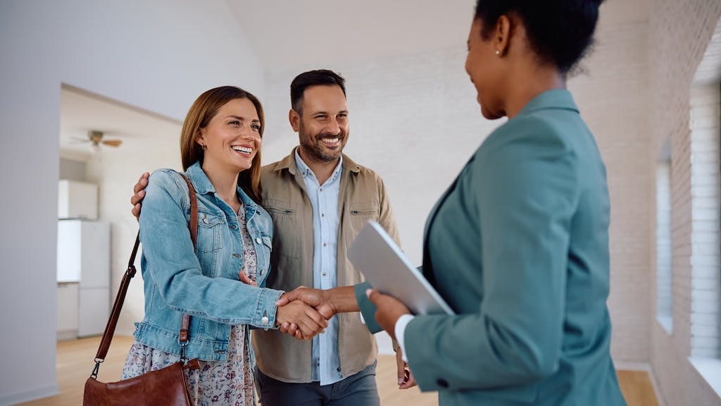 Homebuyers shake hands with a real estate agent who is showing them a home to buy.