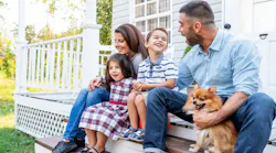 A family sits outside on the front porch of their home