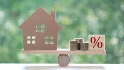 A model home sits on one side of a balancing beam while coins and a block with a percentage symbol sit on the other. A model home sits on one side of a balancing beam while coins and a block with a percentage symbol sit on the other.