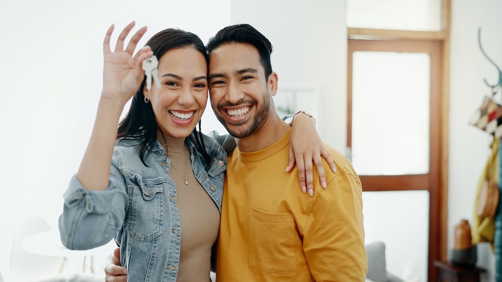 A smiling couple holds up a pair of keys to their new home