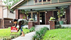 A woman places a 'For Sale' sign in the front yard of a home A woman places a 'For Sale' sign in the front yard of a home