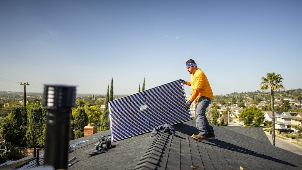 A worker pulls a solar panel onto a roof of a home