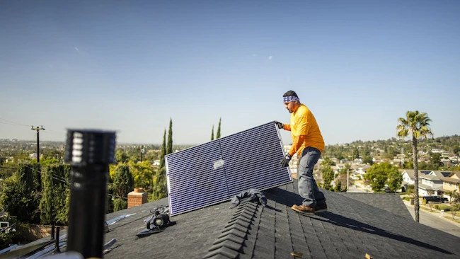 A worker pulls a solar panel onto a roof of a home