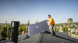A worker pulls a solar panel onto a roof of a home