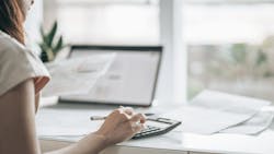 A single woman uses a laptop and calculator to go over her bills A single woman uses a laptop and calculator to go over her bills