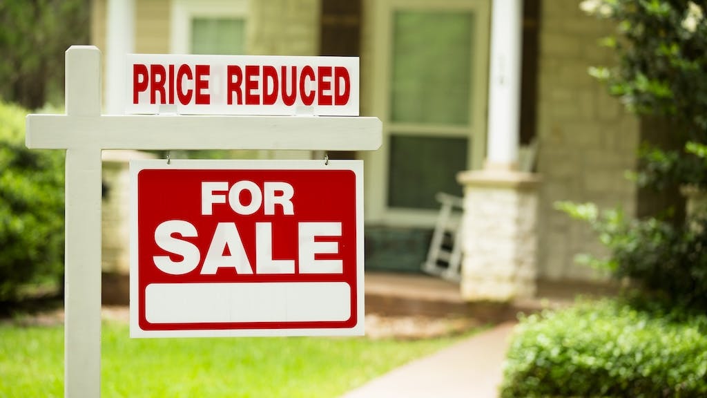 A sign in front of a house shows that the for-sale price has been reduced