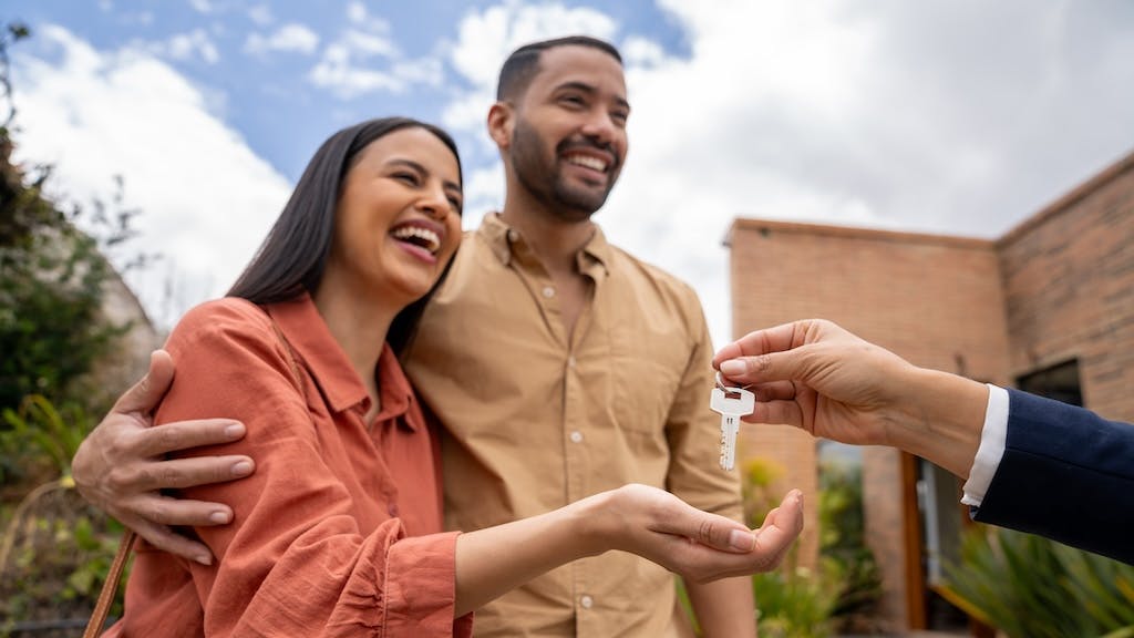 A smiling couple is handed a pair of house keys by their real estate agent