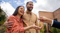 A smiling couple is handed a pair of house keys by their real estate agent