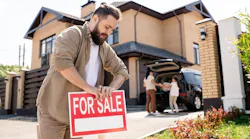 A man sticks a 'For Sale' sign into his front lawn