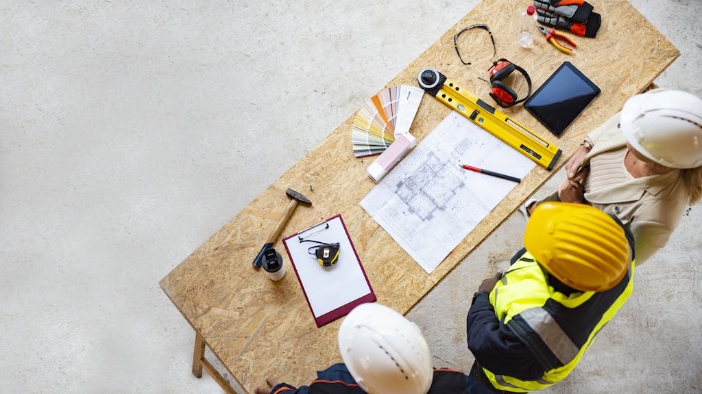 An aerial view of three construction workers looking down at a table with home building plans
