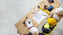 An aerial view of three construction workers looking down at a table with home building plans