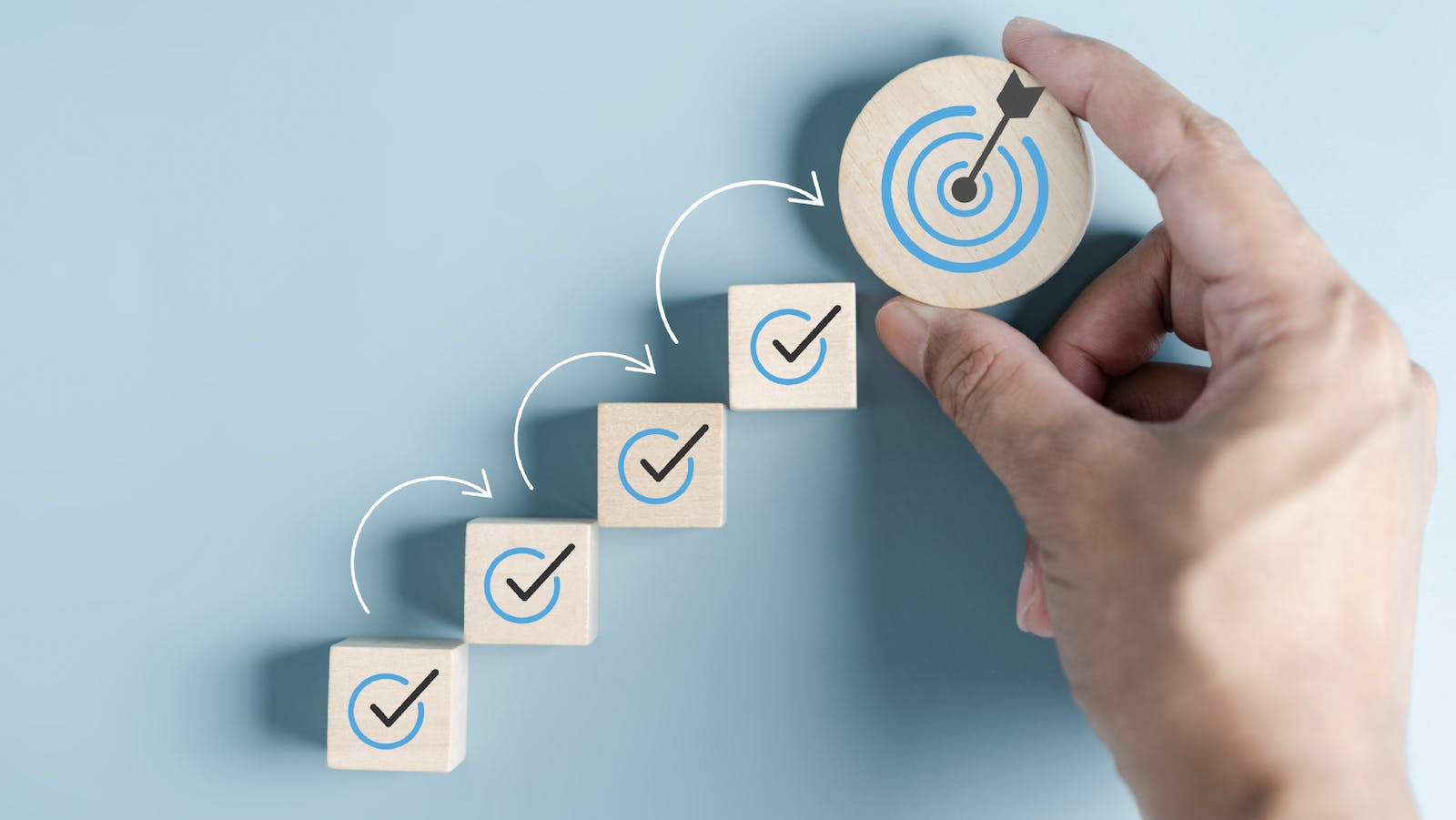 Ascending wood blocks show check-marked steps leading to achieving a business goal