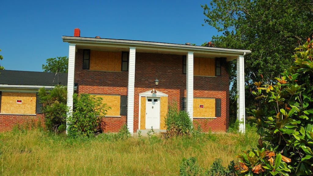 A boarded up suburban home with a foreclosure notice on the windows