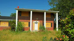 A boarded up suburban home with a foreclosure notice on the windows