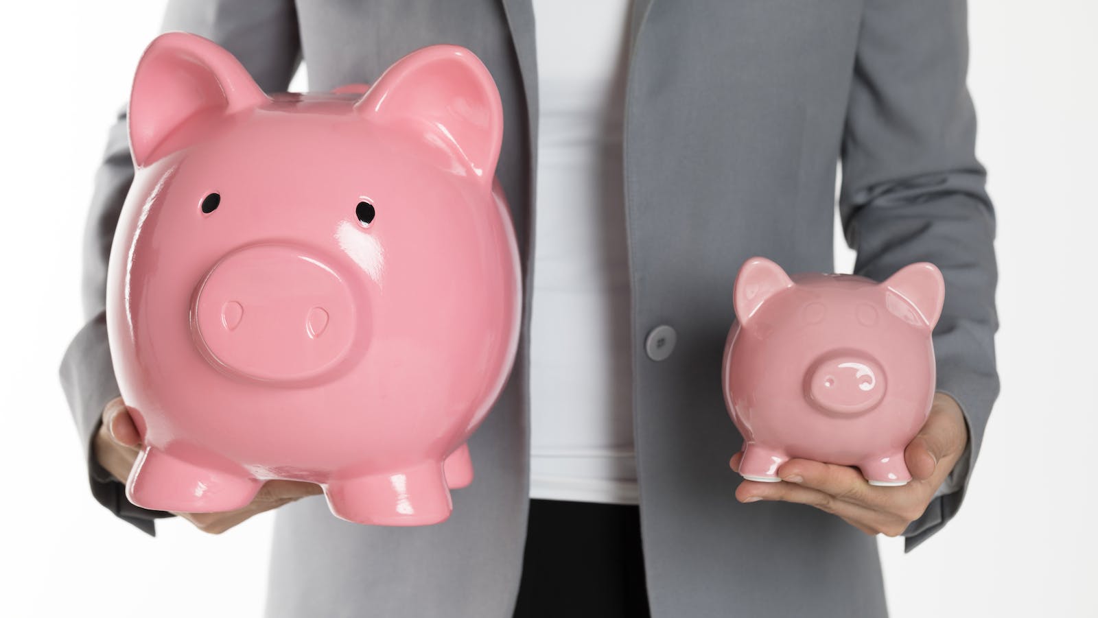 Person holds a large and a smaller piggybank in each hand representing the increase in the amount of a typical down payment for a home