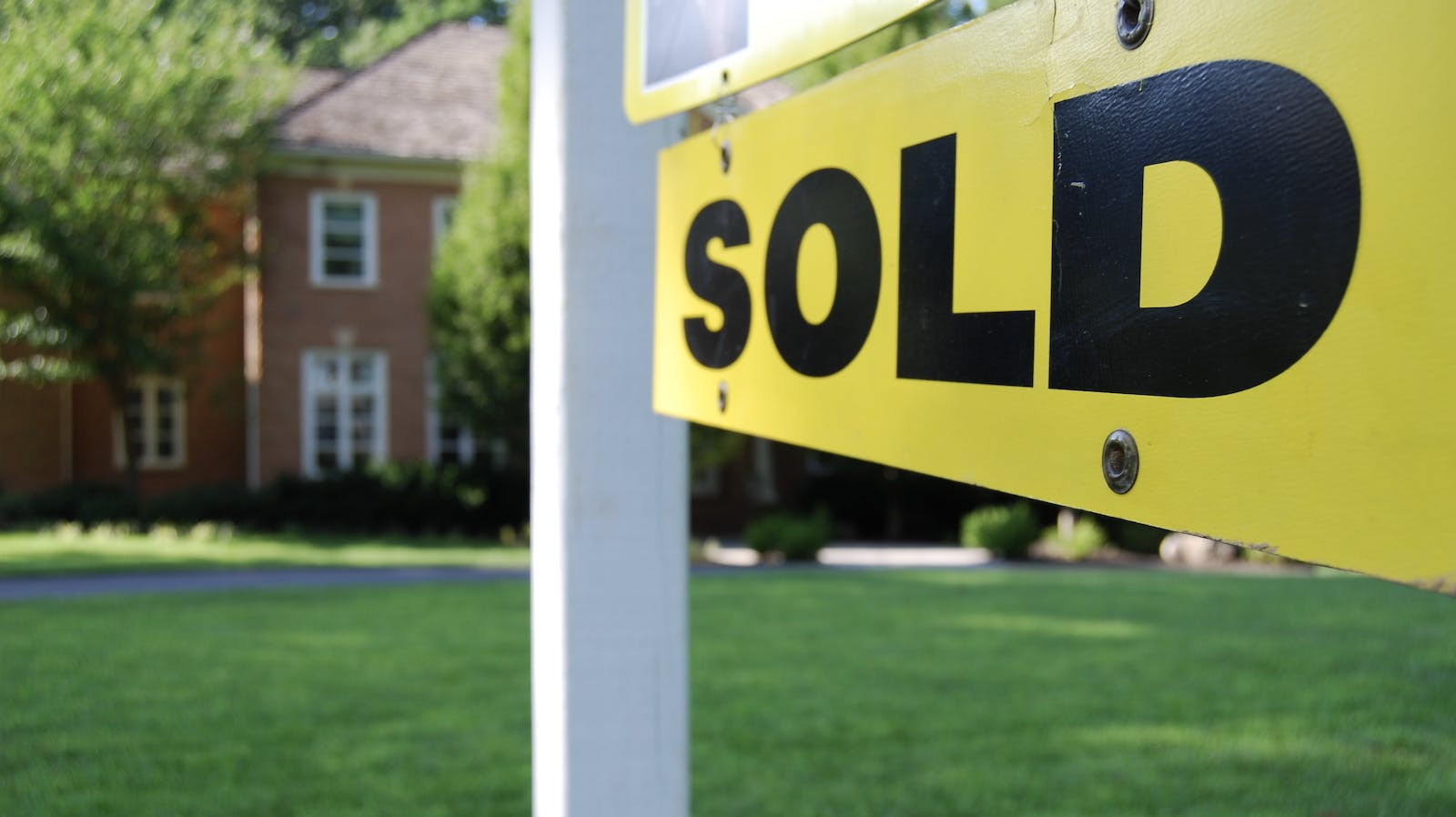 Yellow and black 'Sold' sign in front of an existing home representing the increase in existing home sales prices compared with new-home sales prices