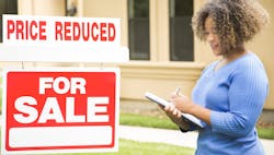 Real estate agent stands near home 'for sale' sign with 'price reduced' notice added on top Real estate agent stands near home 'for sale' sign with 'price reduced' notice added on top