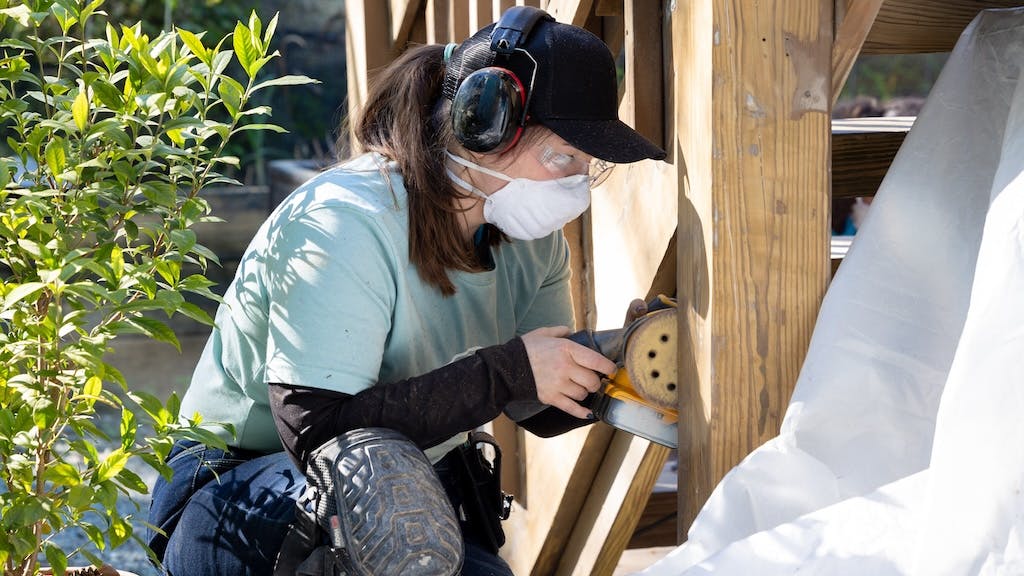 A student works with a sander at a construction site.