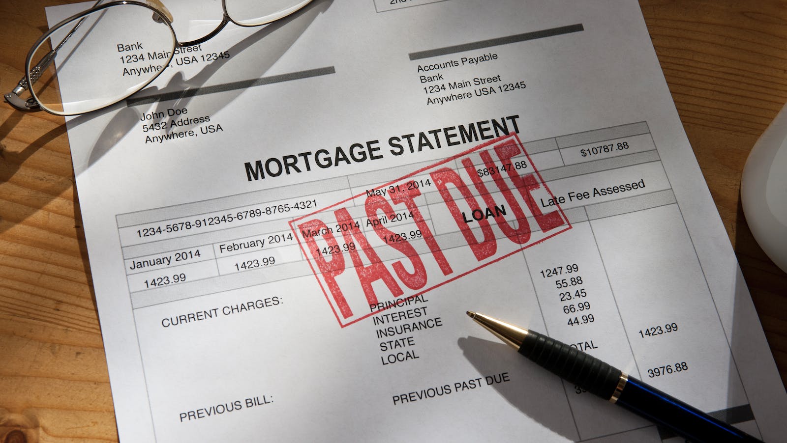 Past-due mortgage statement paperwork with pen and reading glasses on desk