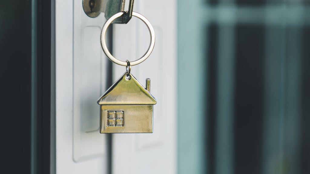 A key with a brass house keyring in the front door of a home represents pending home sales, which declined in January 2025