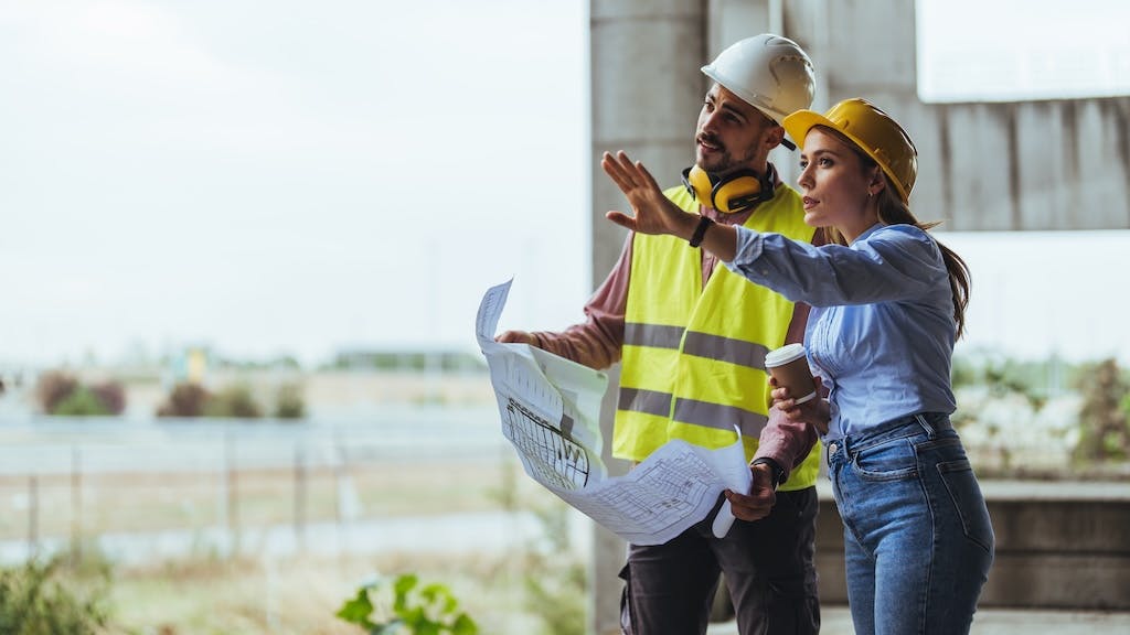 Two construction workers looking over plans at a jobsite as the construction sector sees steady job growth