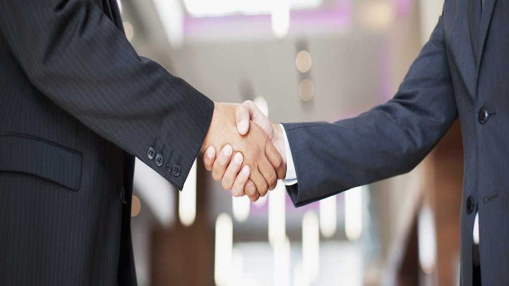 Two businessmen shaking hands represents business deal between Rocket Companies and Redfin