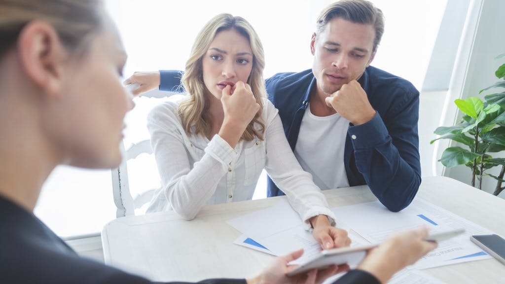 A couple looks stressed as they speak with a real estate agent about buying a home