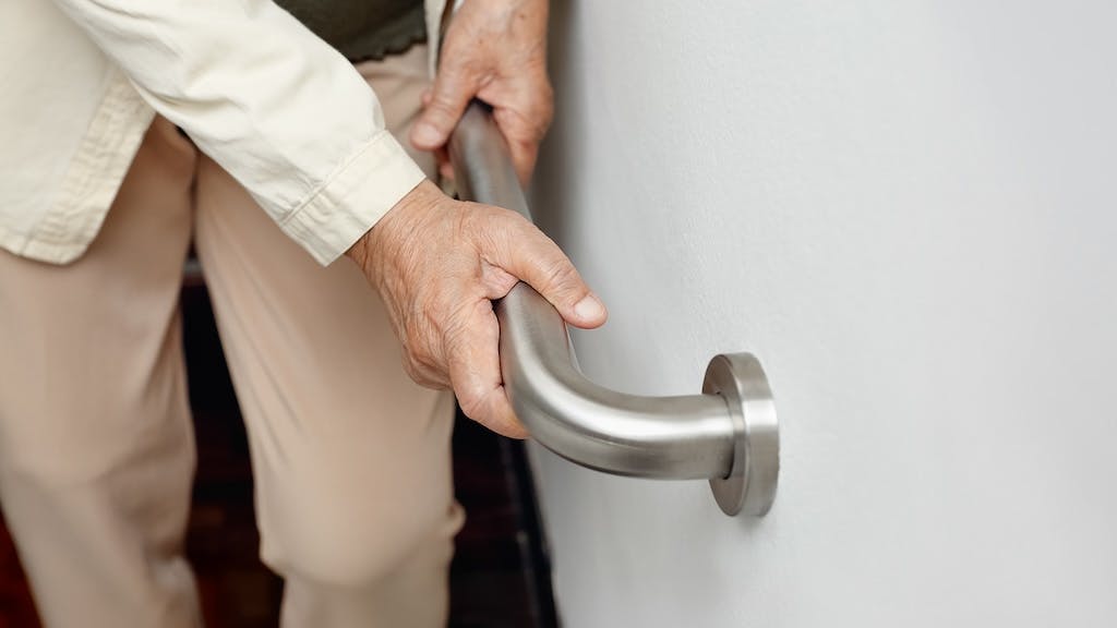 An older adult uses a grab bar mounted to the wall in a home equipped to allow the homeowner to age in place.