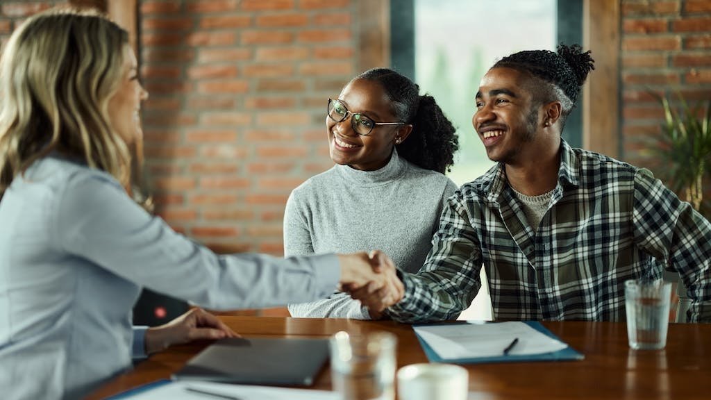 Gen-Z couple shake hands with a real estate agent as they purchase a home.