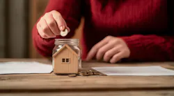 A woman places coins in a jar with a model home in it, indicating saving for a home down payment.