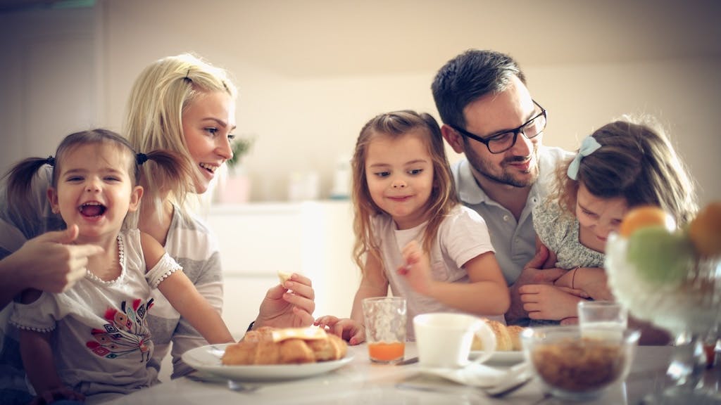 A couple with three small kids eating breakfast together.