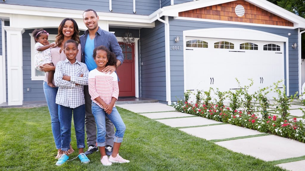 A black family stands in front of a house, representing minority homeownership.