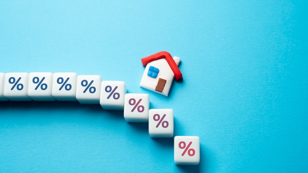 A model home sits above cubes with percentage symbols on them, indicating a change in mortgage rates