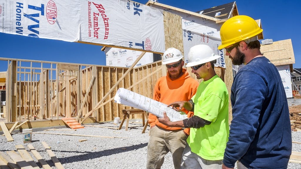 Three construction workers work on a home jobsite with a roll of house plans.