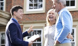 A salesperson meeting with prospective homebuyers in front of a brick house. A salesperson meeting with prospective homebuyers in front of a brick house.
