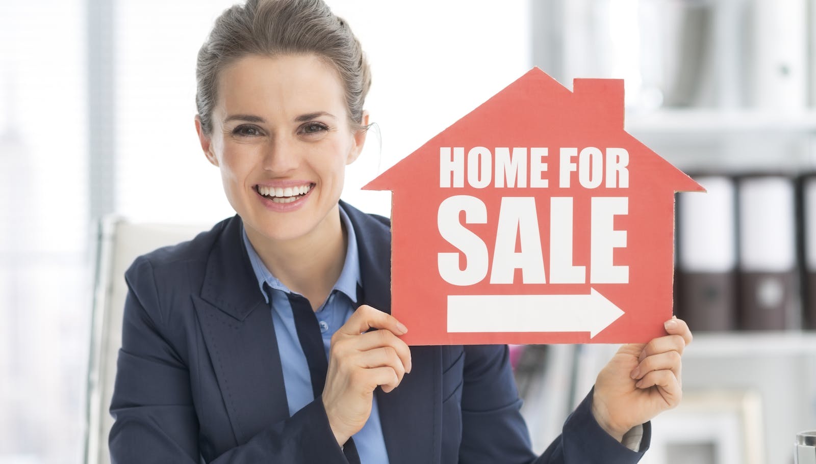 New-home salesperson holds up home for sale sign.