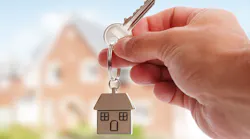 A home seller holding a key with a house in the background