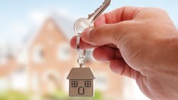 A home seller holding a key with a house in the background A home seller holding a key with a house in the background