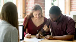 In the process of buying a new home, a couple signs documents excitedly with a real estate agent