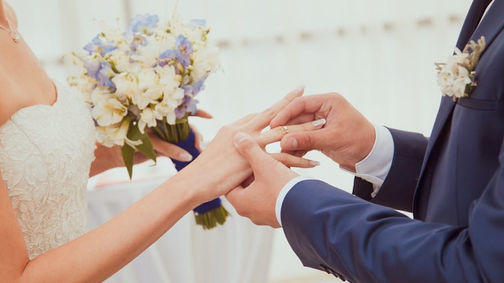 A groom places a wedding band on the bride's ring finger