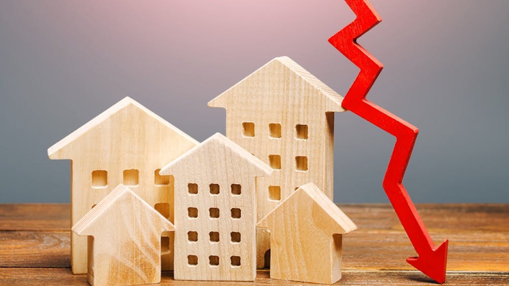 An arrow descending next to several wooden model homes indicates falling home prices