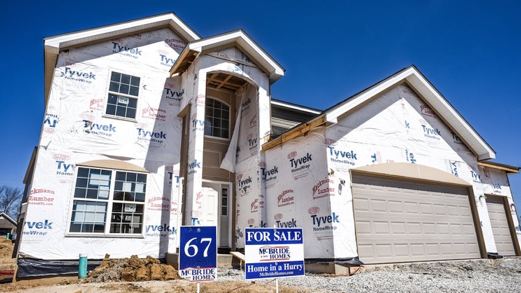A newly built home with a 'For Sale' sign in the front yard