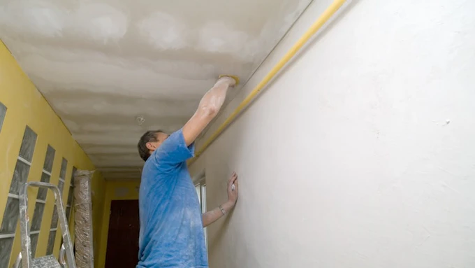 Young homeowner sands down spot on hallway ceiling in a fixer-upper home