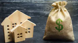 Model wooden homes sit next to large bag of money, indicating the surge in housing costs