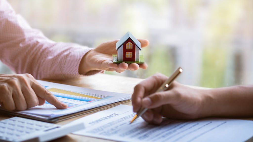 A homebuyer signs papers with a real estate agent